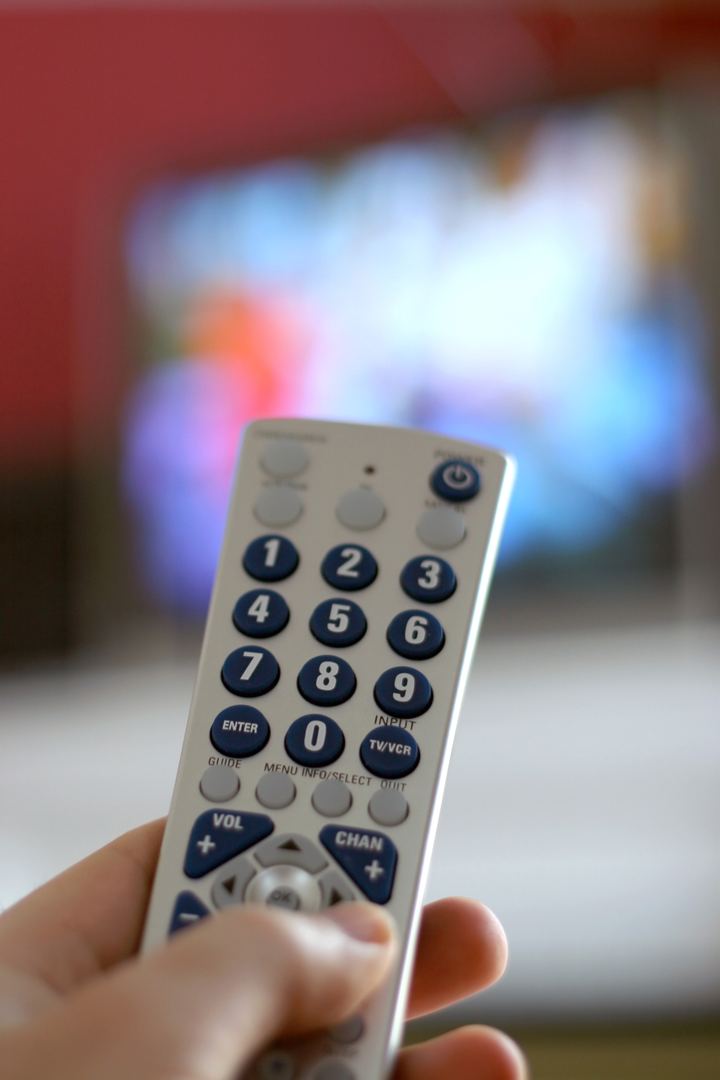 Hand mit Fernbedienung vor einem Fernseher – Fernsehtechnik von TV4YOU in Wien